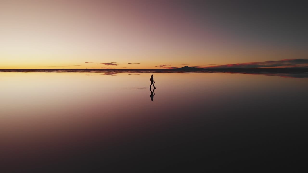 Aerial of a lone figure walking along the mirrored reflection of the world's largest salt flat at dusk in Uyuni Salt Flats , Bolivia