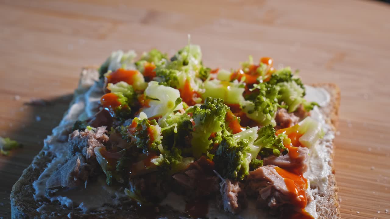 chorreando salsa picante roja sobre un sándwich de tostadas anabólicas con atún y brócoli