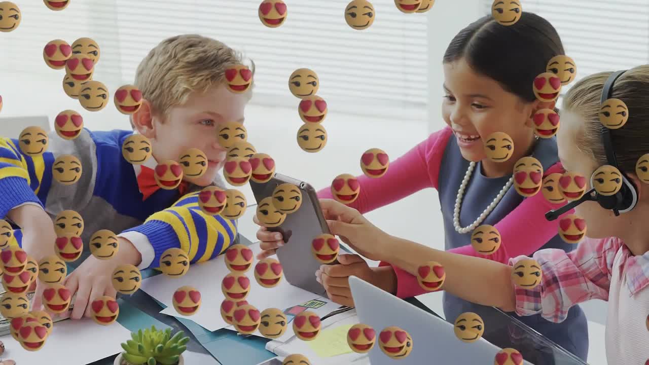 Multiple face emojis floating against group of kids using digital tablet