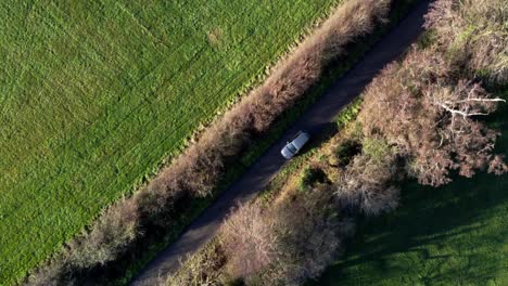 aerial top down shot, grey car driving down an english country road, surrounded by trees