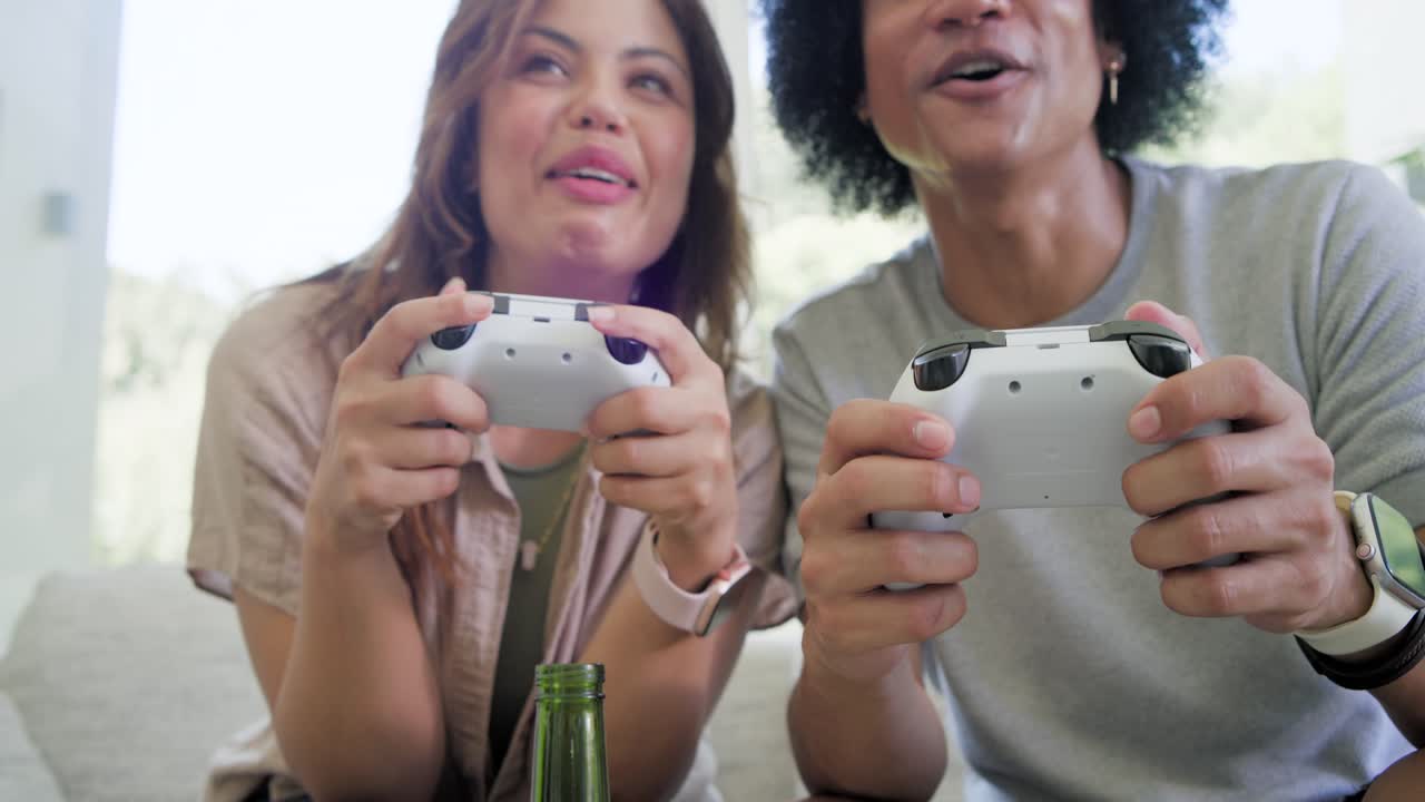African American couple holding controllers, reacting to on-screen win on couch with green bottle