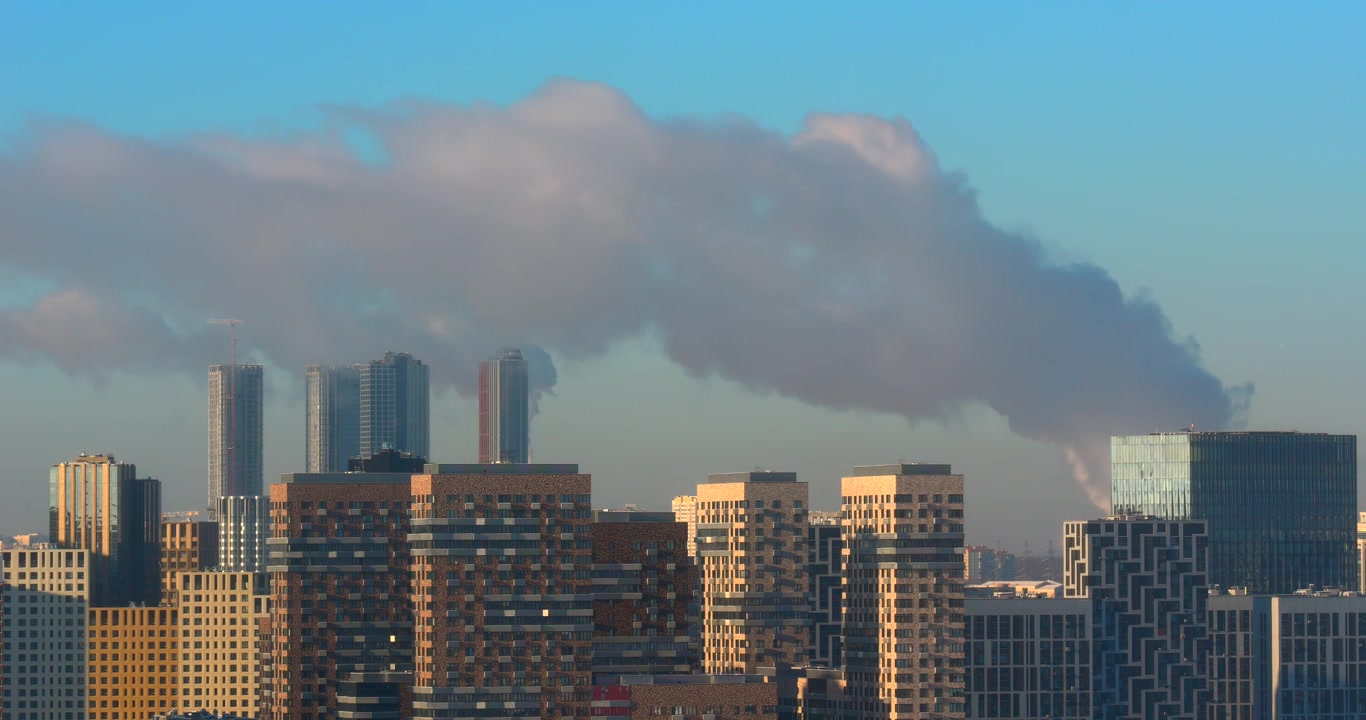 Urban skyline shows factory smoke drifting behind modern high rise buildings under blue sky for air pollution industry environment and city development themes