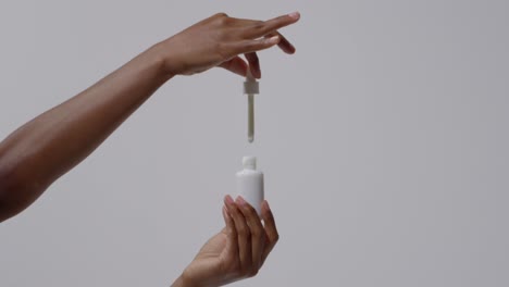 close up of woman squeezing dropper of beauty product from bottle on white background in slow motion