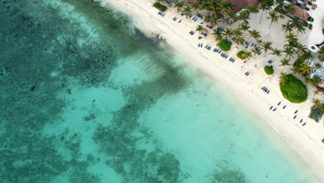 Vista-Aérea-De-Un-Dron-Giratorio-De-Una-Hermosa-Playa-Tropical-De-Vacaciones-Con-Agua-Azul-Cristalina,-Arena-Blanca,-Palmeras,-Tumbonas-En-Un-Resort-En-Riviera-Maya,-México-Cerca-De-Cancun