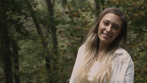 Woman-standing-in-the-woods-turns-and-looks-at-camera-trees-natural-setting