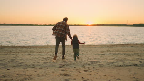 Vater-Und-Sohn-Halten-Sich-An-Den-Händen-Und-Rennen-Bei-Sonnenuntergang-Zum-Fluss.-Glückliches-Familienwochenende