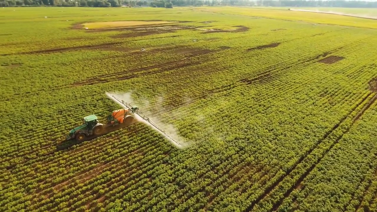 Trattore che irrora pesticidi, insetticidi ed erbicidi su un grande campo agricolo.