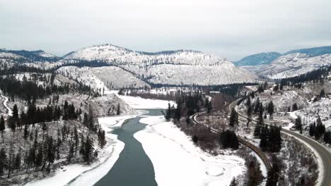 Breite-Luftaufnahme-Von-Fahrzeugen-Und-Transportzügen-Auf-Dem-Yellowhead-Highway-5-Und-Eisenbahn-Durch-Teilweise-Zugefrorenes-North-Thompson-River-Valley-In-Der-Nähe-Von-Kamloops,-Verschneite-Landschaft-Panoramaaussicht