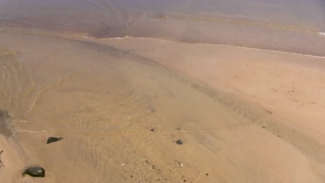 lentamente panorámica de mirar hacia abajo en una playa de arena a aguas más profundas y un paddleboarder