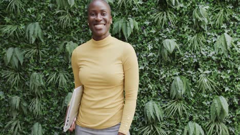 Portrait-of-happy-african-american-businesswoman-holding-laptop,-smiling-in-garden,-slow-motion