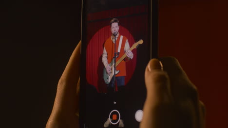 close up view of smartphone held by hands recording a male musician playing guitar and singing during live music perfomance