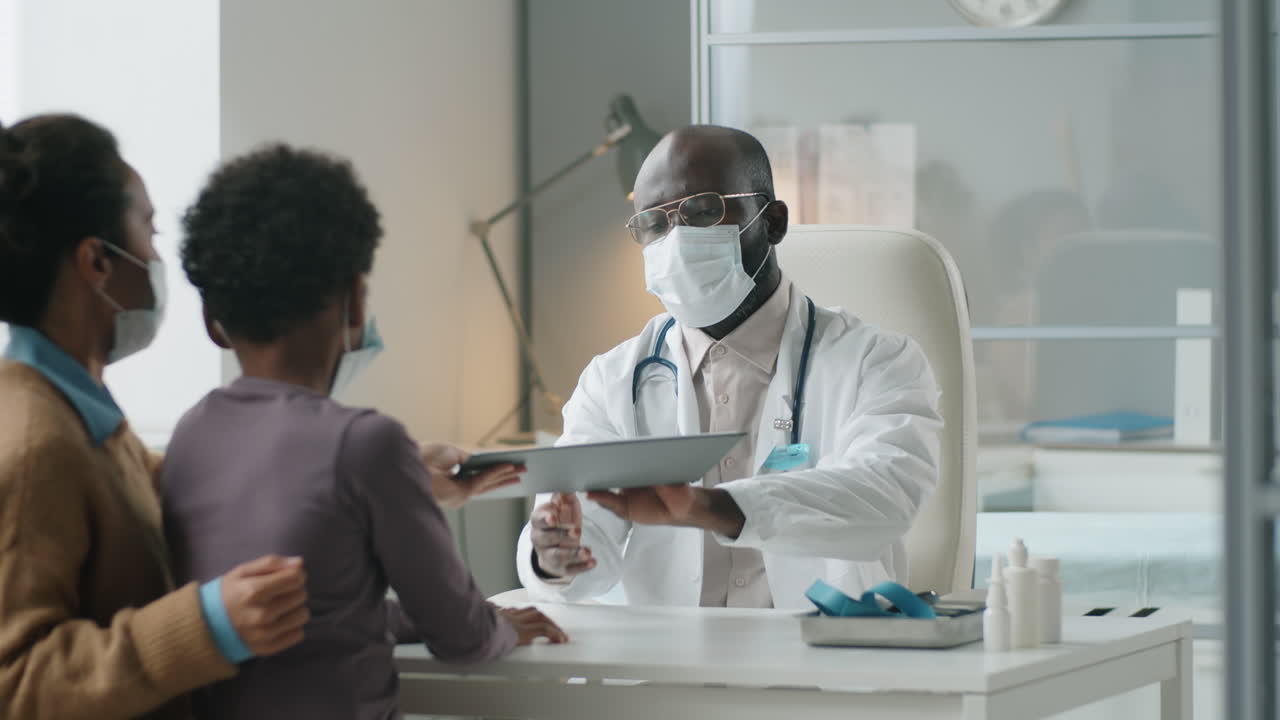 Black Pediatrician in Mask Giving Consultation to Boy and His Mother