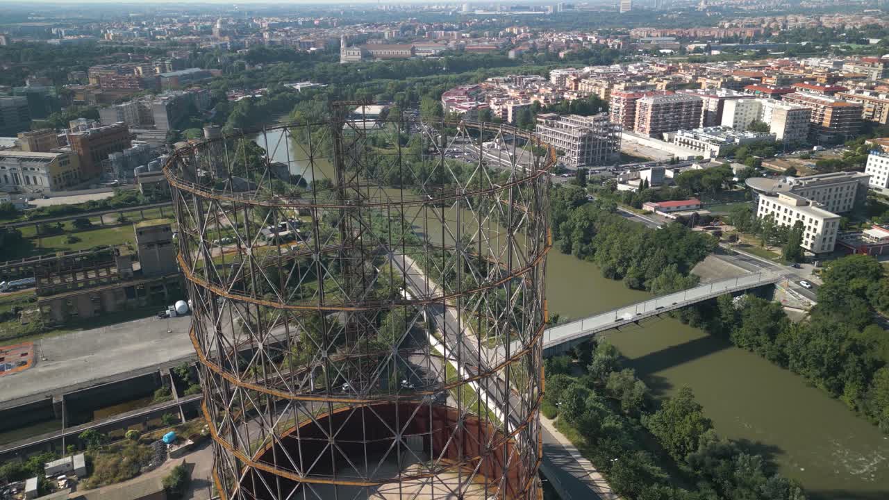 una toma aérea de un dron volando alto sobre una vieja estructura de hierro, gazometro en el distrito de ostiense, roma, italia con la vista de la ciudad en el fondo
