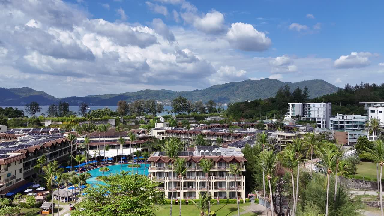 Drone footage captures a luxury resort in Phuket, Thailand, showcasing pools, lush greenery, and scenic mountain views under bright daylight
