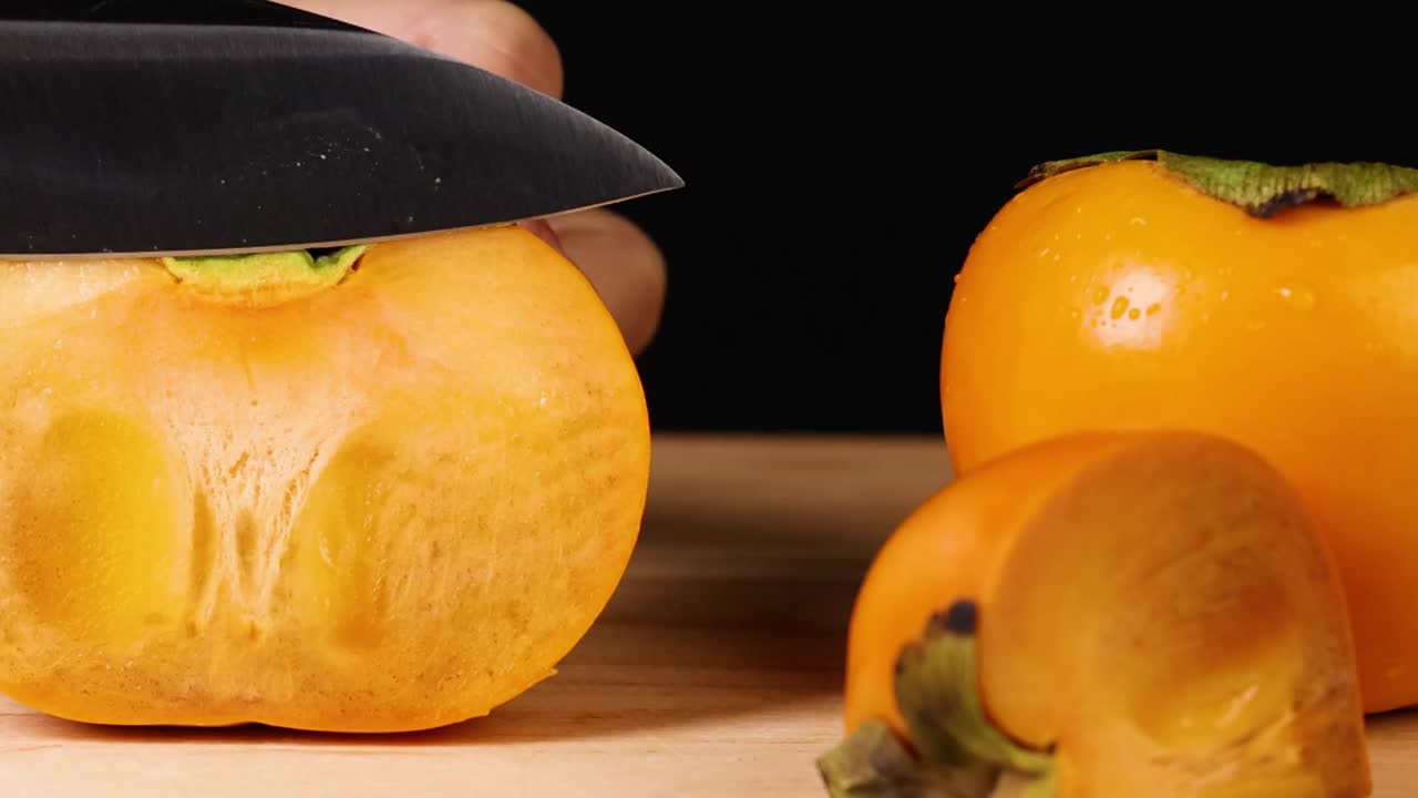 Sebuah pisau tajam memotong buah kesemek oranye terang dalam bidikan makro yang detail