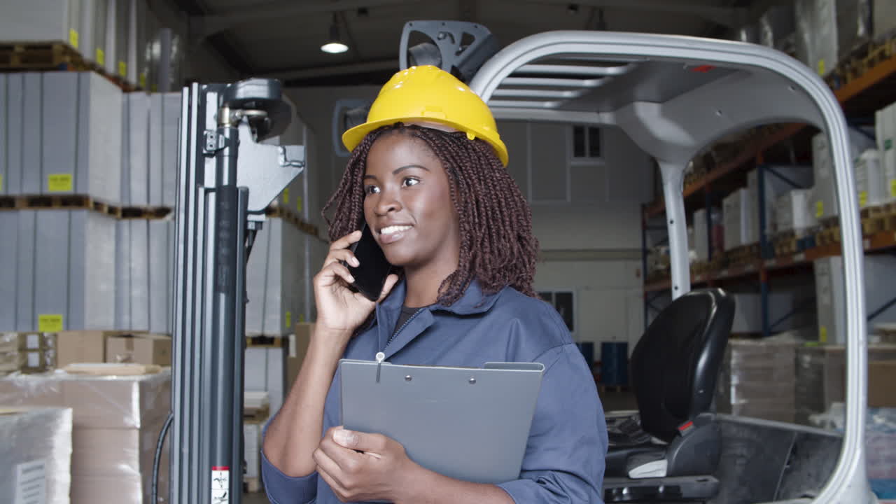 African American female worker talking on phone, standing in storehouse and holding a clipboard