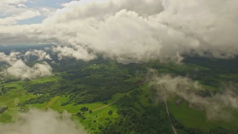 green vibrant landscape with forest and fields, fly above cloudscape