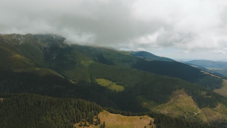 aerial view showing layered mountain ranges covered by low altitude clouds, dense forests and vibrant green pastures