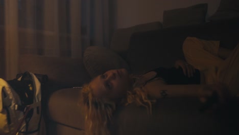 close-up of a tired blonde woman in a black t-shirt lying on a gray sofa and looking at the ceiling during late night sleeplessness