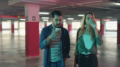 young caucasian and stylish man and woman walking in a empty parking and talking while drinking coffee