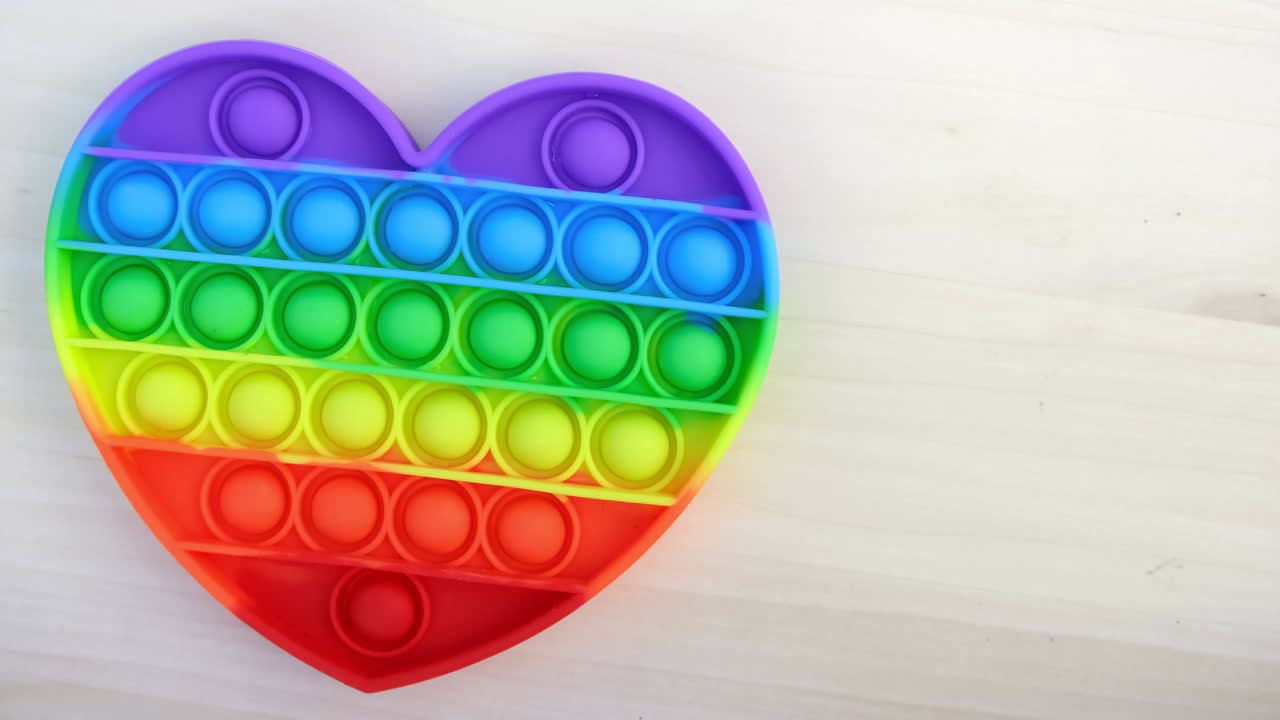 pop it o simple hoyuelo girando alrededor. vista superior de un popit girando sobre un fondo de madera. juguete sensorial antiestrés de silicona. tendencia 2021. pop it - juguete colorido y reutilizable para aliviar el estrés. en forma de corazón.