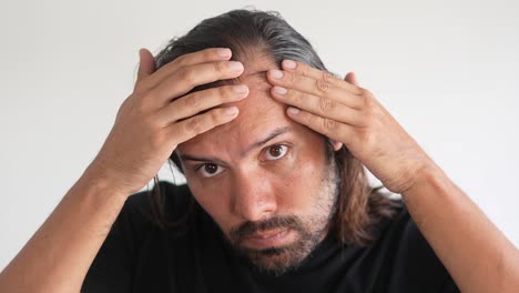 hombre latino comprobando su cabello con línea de cabello retrocediente y calvicie, densidad de cabello