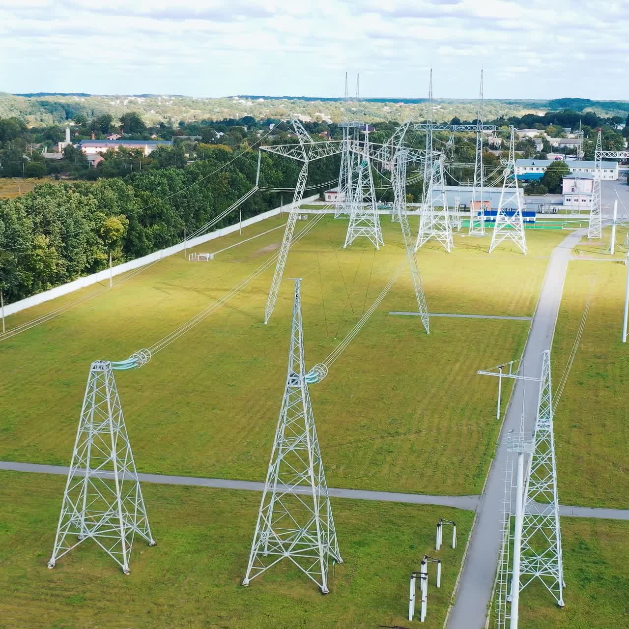 Electricity pylons in the countryside. Power station with white tall towers on field. Distribution of electricity. Motion camera back