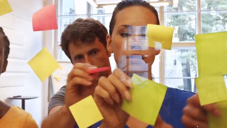 male and female business executives sticking sticky notes on glass