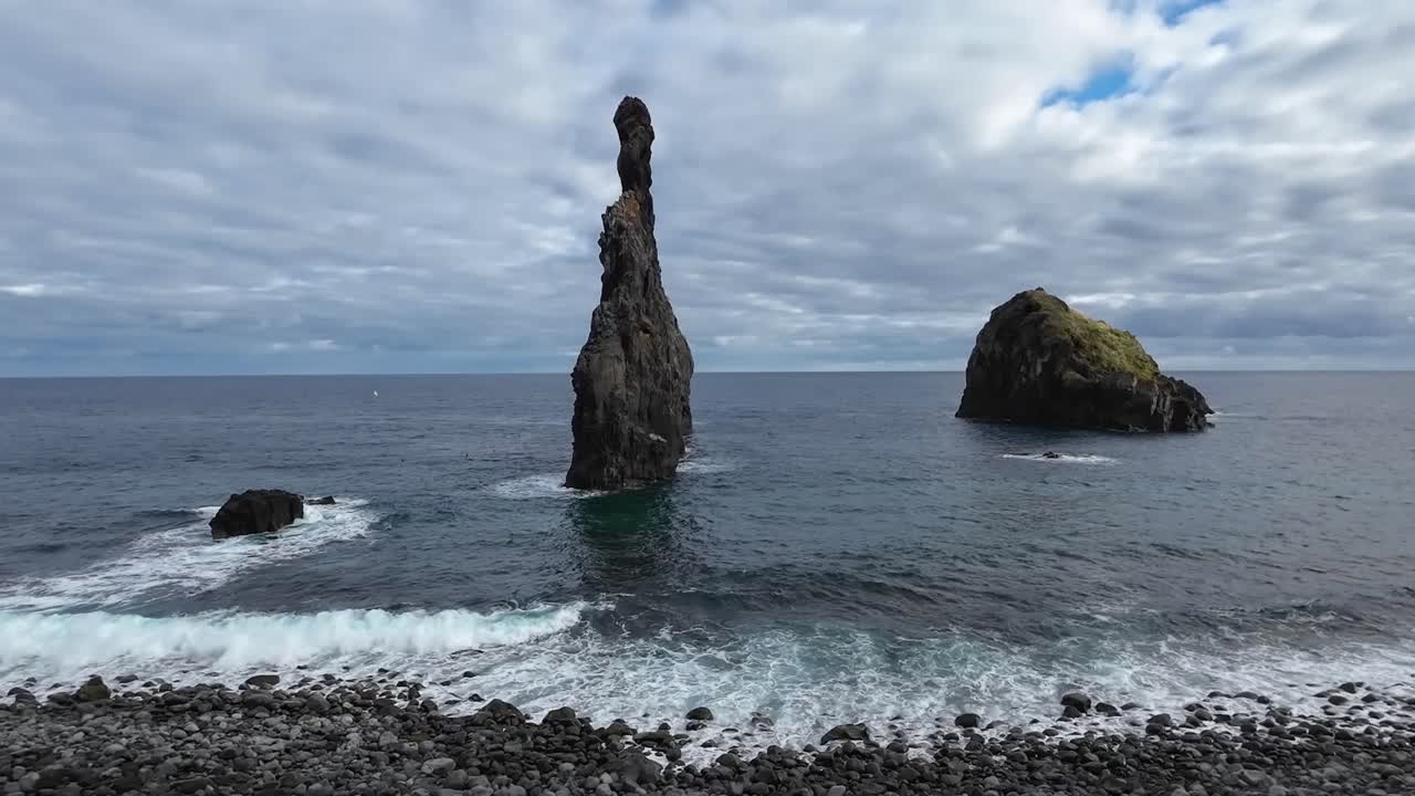 formaciones de piedra de pie en el océano y el mar con olas que pasan por entrar en la playa de piedra empedrada en un día nublado