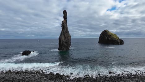 Stone-formations-standing-in-the-ocean-and-sea-with-waves-passing-by-entering-the-cobble-stone-beach-on-a-cloudy-day