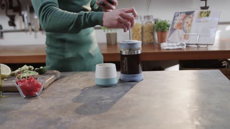 Midsection-of-caucasian-man-making-coffee-and-using-smartphone-in-kitchen,-slow-motion