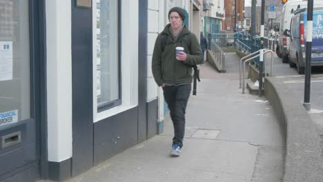 man walking with coffee along street on cold day