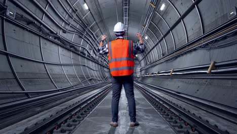 full body back view of a male engineer with safety helmet raising his hands celebrating while working in underground subway tunnel