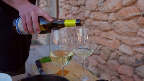 sirviendo vino blanco español en dos copas con una pared de piedra de estilo mediterráneo en el fondo