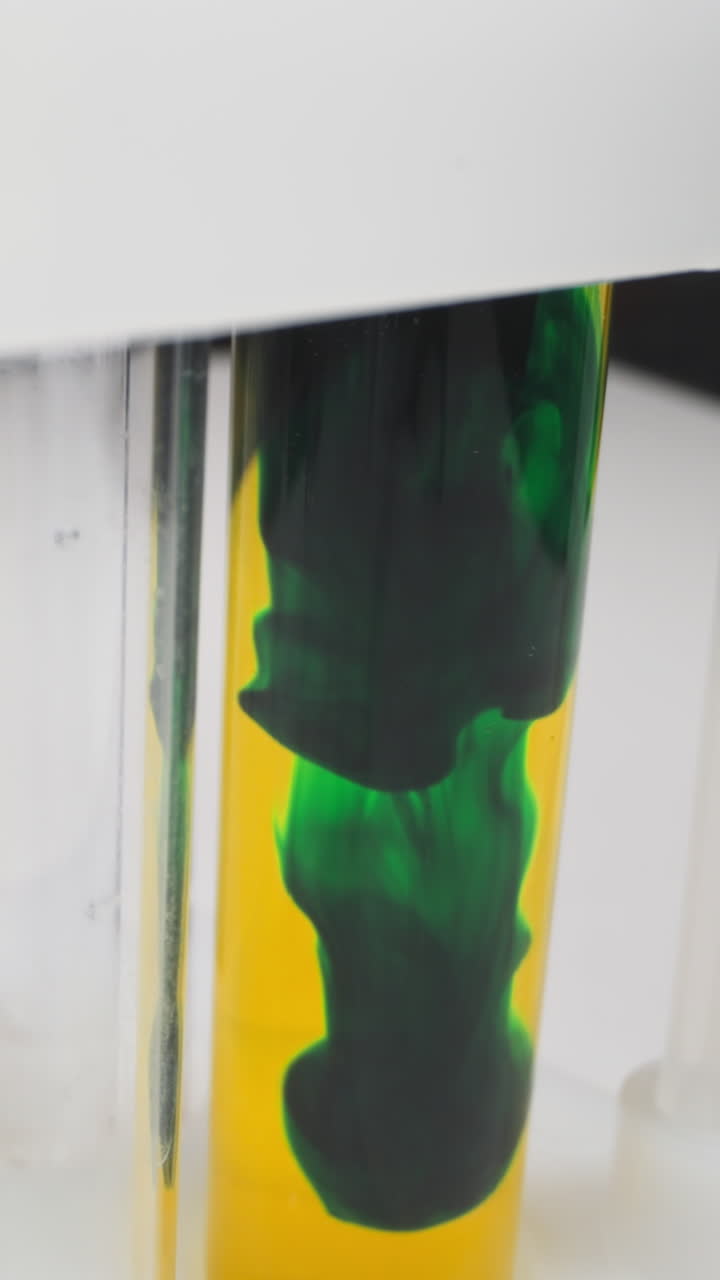 Diffusion of dark green paint settling down in test tube with yellow liquid on rack in laboratory slow motion. Probe lens shot of chemistry research macro