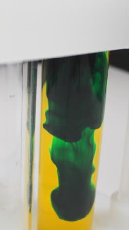 diffusion of dark green paint settling down in test tube with yellow liquid on rack in laboratory slow motion. probe lens shot of chemistry research macro
