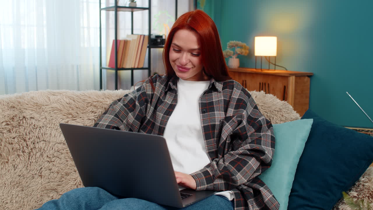 Woman sitting on sofa shopping online with laptop choosing dress touching chin in thoughtful pose