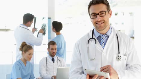 médico usando la tableta mientras el personal está trabajando detrás de él
