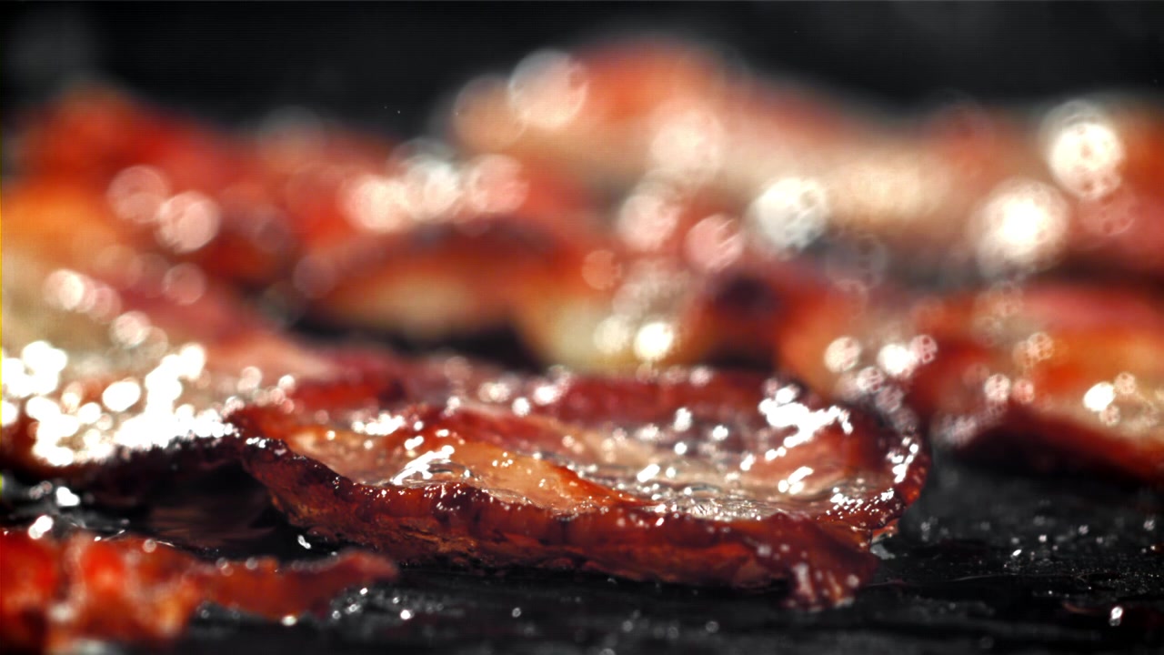 Deliziose striscioline di pancetta che sfrigolano e friggono su una padella calda