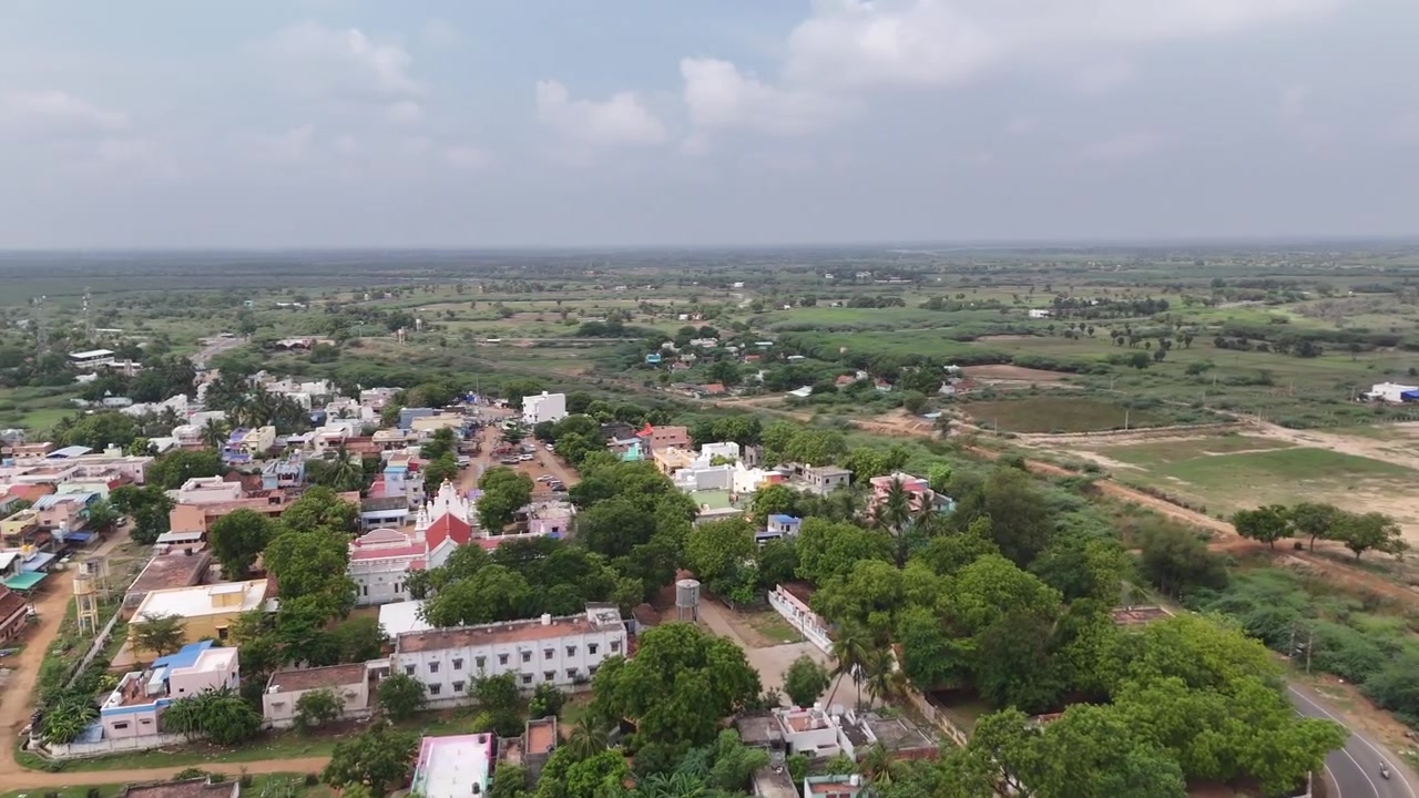 Vista aerea cinematografica di un pittoresco villaggio vicino a Karaikkudi, che mostra case colorate, strade alberate, templi e vasti campi agricoli. Il paesaggio riflette il tranquillo fascino rurale