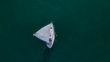 Birdseye-view-of-sailboat-cruising-through-green-blue-ocean-water