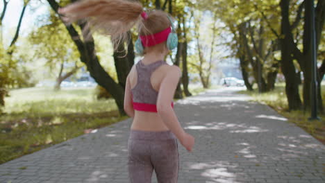 back view of athletic sport runner toddler girl training marathon run, listening music in headphones