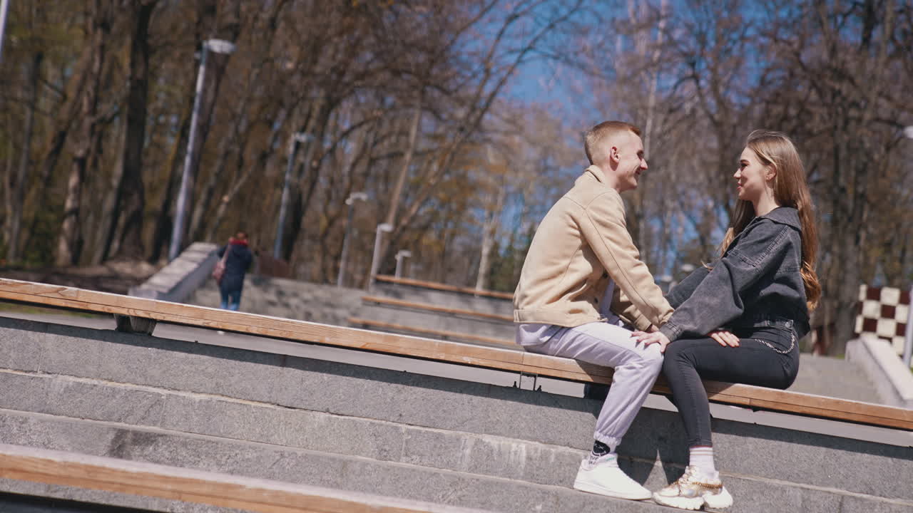 Happy boy and girl sitting in front of each other at the bench at the park. Couple in love spending time with each other at the street at the romantic date. Enjoying the time together concept