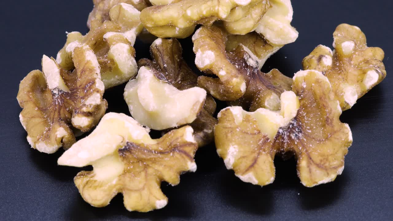 Handful of peeled walnuts, rotating close up shot in 4k over black surface background