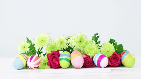 painted easter eggs, bunch of flower and envelope on wooden background