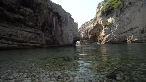 low angle view of still clear water of the sea in a shaded and secluded cove hidden by tall cliffs along the coast of croatia