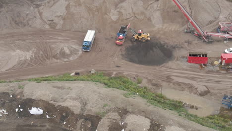 aerial of excavator dumping sand in truck - close