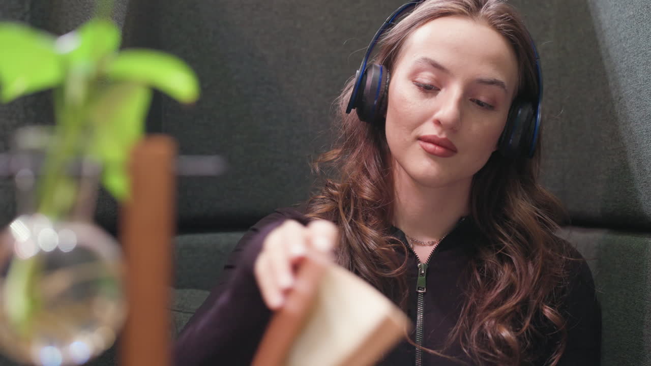 Close up of lady wearing headset with eyes closed, enjoying peaceful moment in cushioned booth and soft lighting enhances relaxed mood while blurred plant in glass vase adds natural ambiance