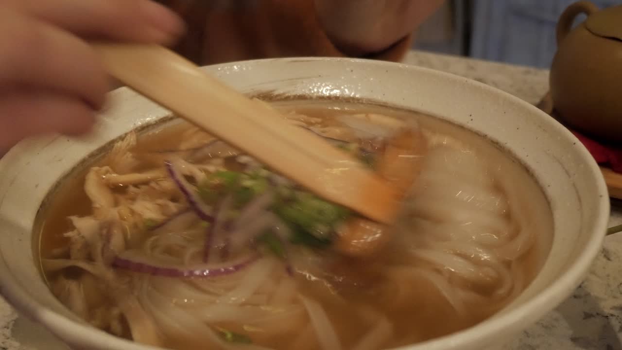 A warm bowl of Vietnamese chicken noodle soup with lime and fresh herbs being garnished