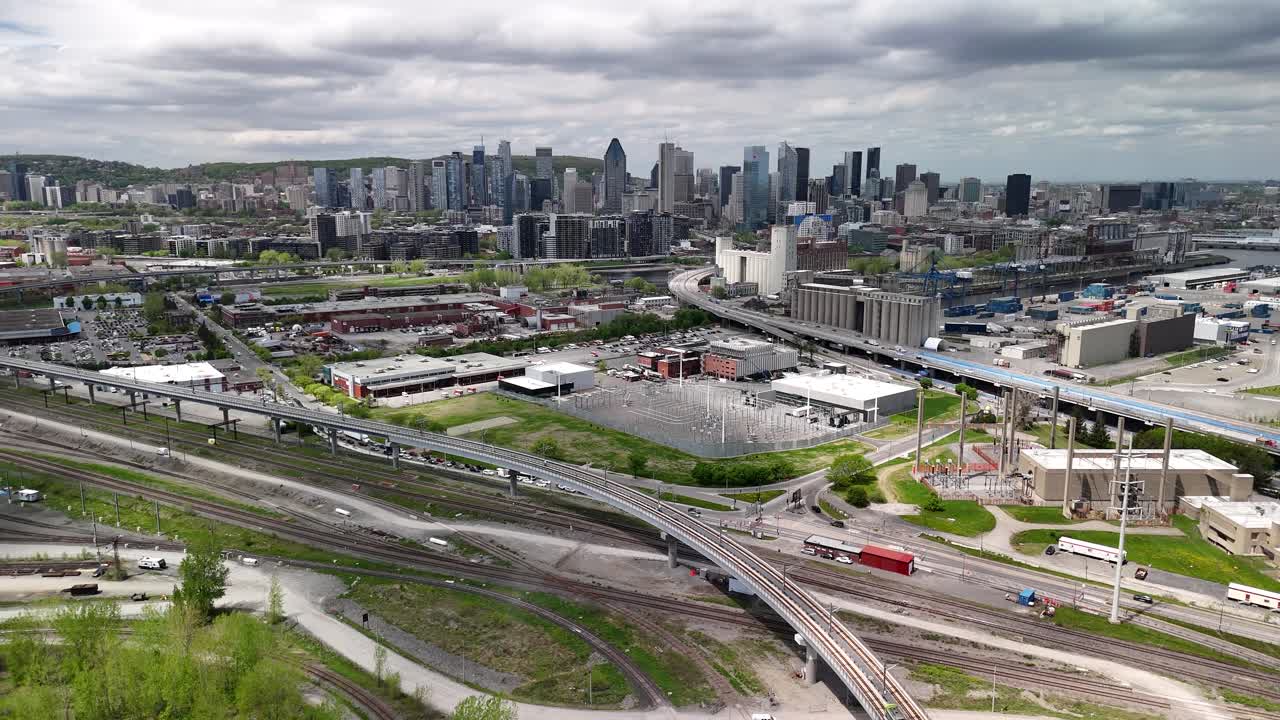 Aerial drone shot of Montreal Skyline, slow zoom out featuring REM train in foreground. Overcast grey sky and urban landscape.